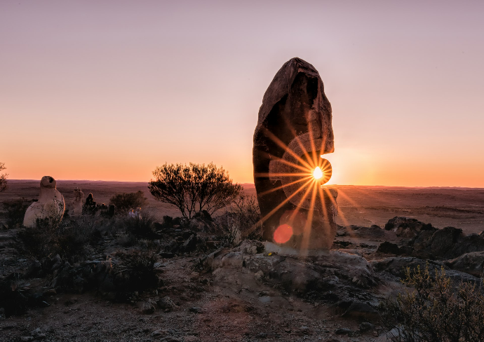 the sun is setting behind a large rock in the desert